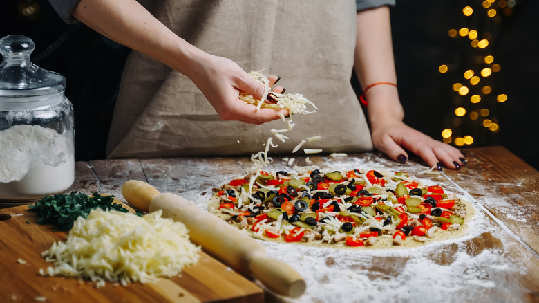 person making pizza with grated mozzarella