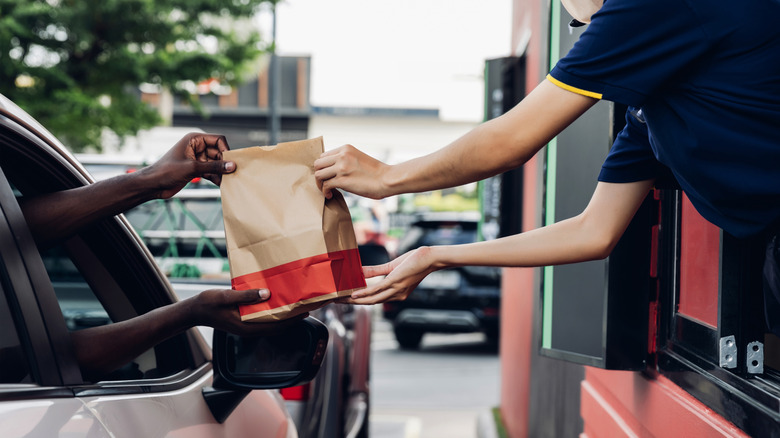 A drive thru employee handing someone in a car a bag of food