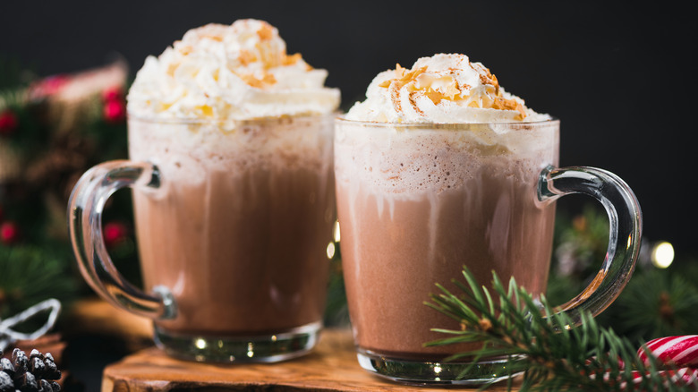 Two glass mugs of hot chocolate piled with whipped cream