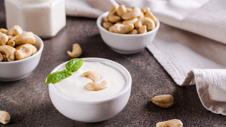 a bowl of vegan cashew sauce next to two bowls of cashews