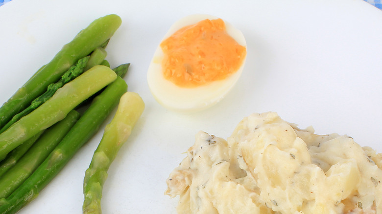 white plate with asparagus, a deviled egg and mashed potatoes