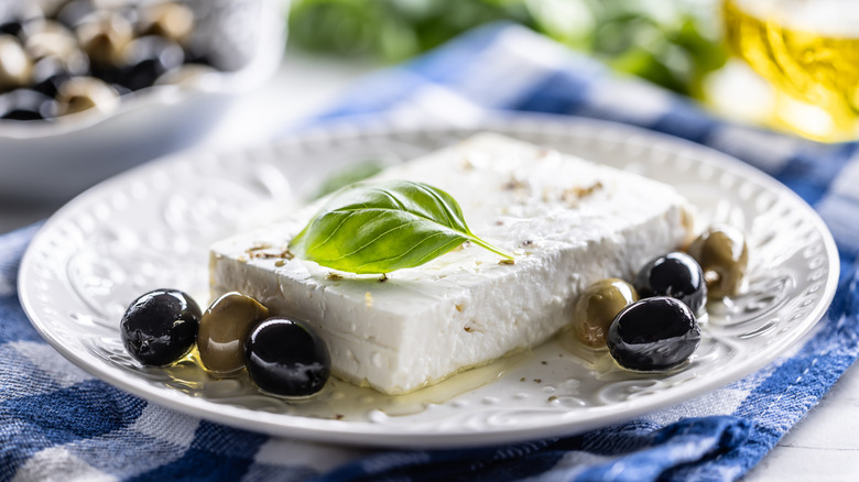 block of feta cheese on plate with basil and olives