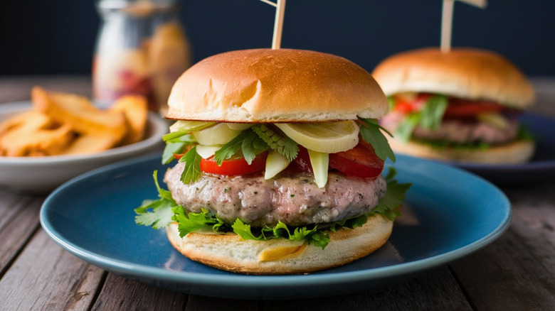 A big, juicy turkey burger with fries and a burger in the background