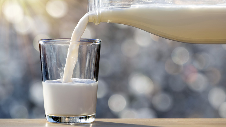 Pouring milk from glass bottle into drinking glass