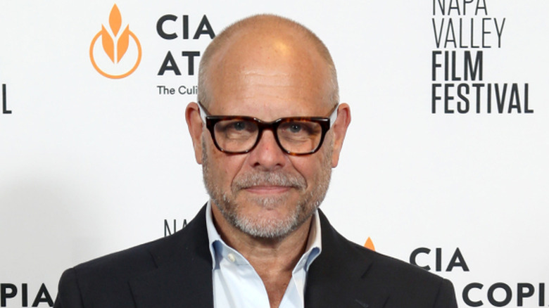 Alton Brown smiles in black blazer, white shirt, and glasses