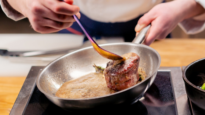 Searing beef roast on a pan, using a ladle to keep the meat from slipping