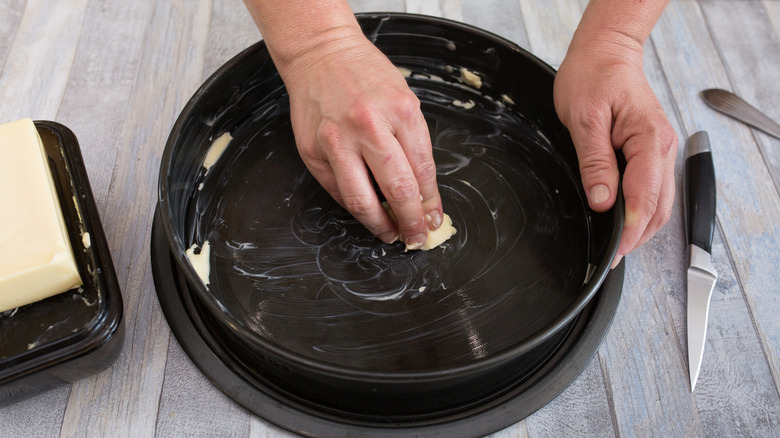 A person greasing a baking dish with butter