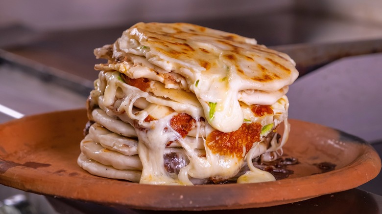 Stack of browned pupusas with melted cheese on a plate