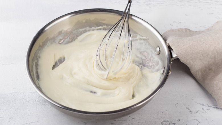 whisking alfredo sauce in a pan