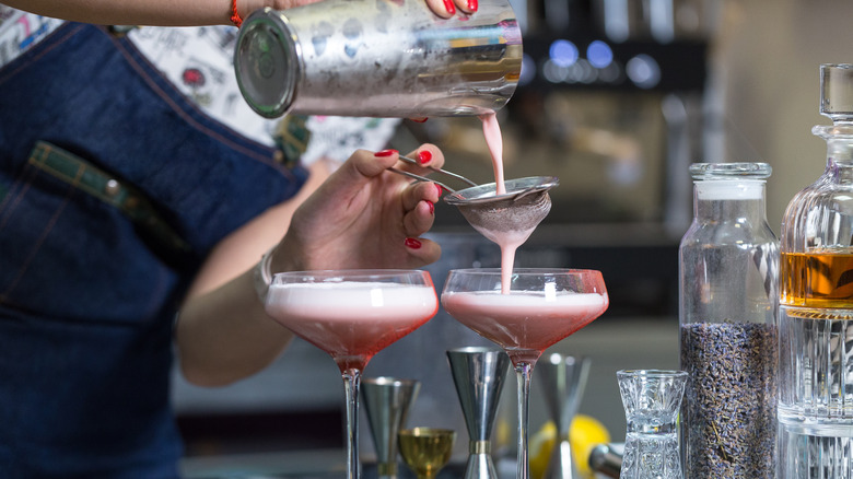 female hands pouring cocktail from a shaker into glasses