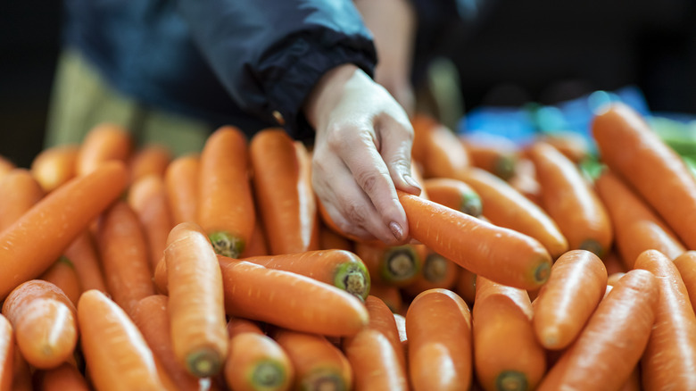 Person shopping for carrots in a grocery store produce section