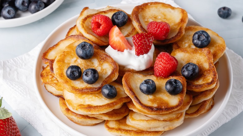 Plate of mini pancakes with berries and a dollop of whipped cream