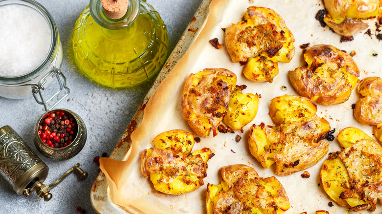 Smashed potatoes on baking tray with parchment, salt, olive oil, and pepper grinder