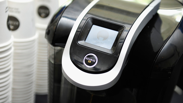 A black and grey Keurig machine with cups stacked next to it