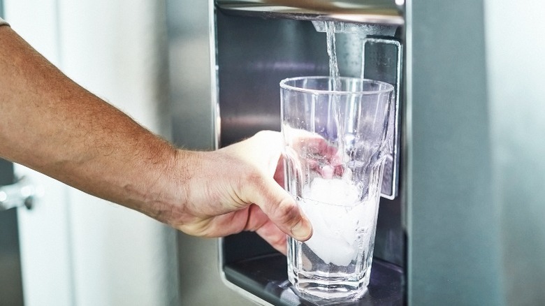 Hand filling water glass from fridge