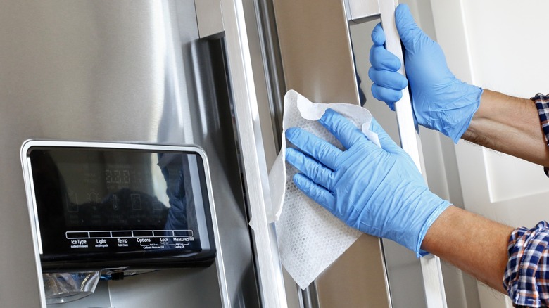 Gloved hands wiping a refrigerator door