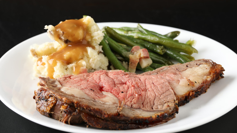 A plate with a slice of prime rib, mashed potatoes and gravy, and green beans