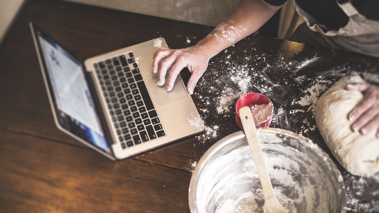 Checking laptop while kneading dough