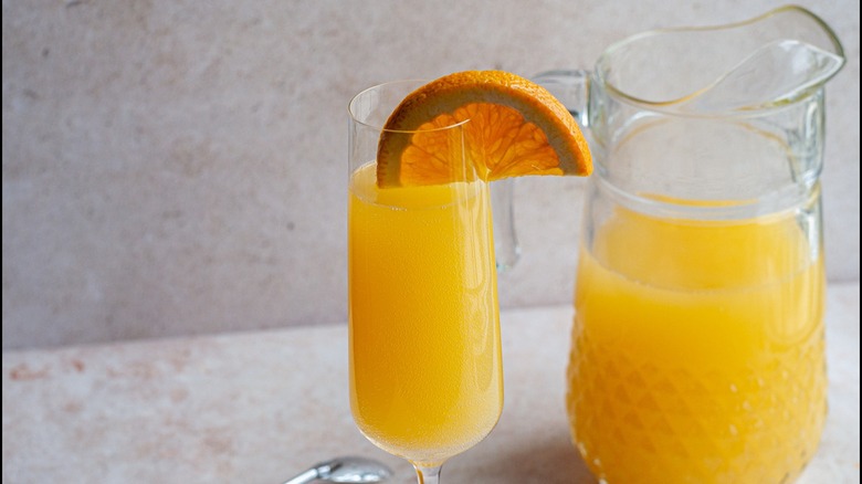 A Mimosa cocktail next to a full pitcher