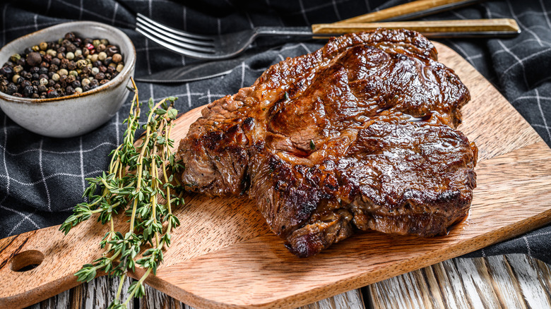 Smoked chuck roast resting on a wooden board with greens and silverware