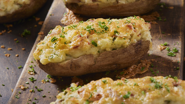 Several baked jacket potatoes on wooden surface with seasonings