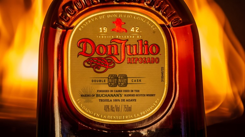 Close-up of a bottle of Don Julio reposado tequila against a dark background with flames