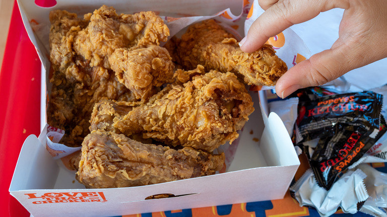 Foodie grabbing a piece of fried chicken from a Popeye's takeout box