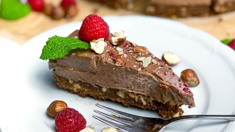 A slice of no-bake chocolate cheesecake with raspberries, hazelnuts, and a mint leaf