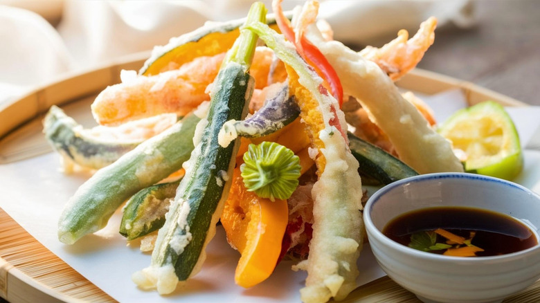 Colorful plate of zucchini and other vegetable tempura stacked into pyramid with dipping sauce on the side