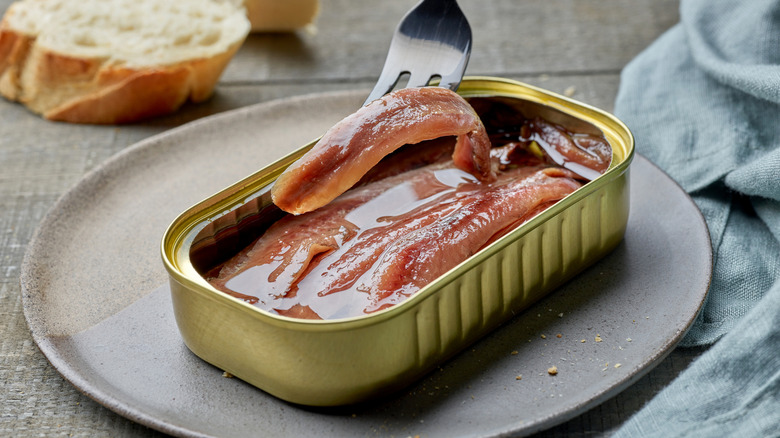 a tin of anchovies on a plate with a fork lifting one out