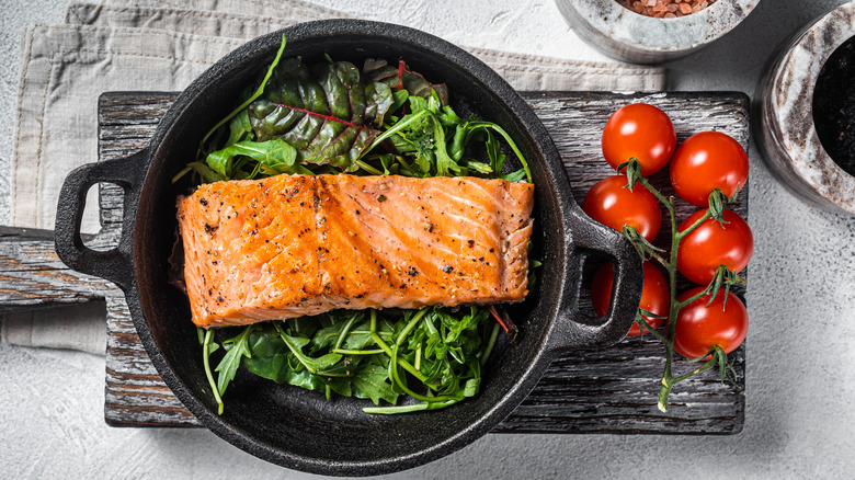 Salmon filet in saucer with greens and tomatoes on the side