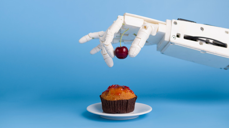 A robotic arm placing a cherry on a cupcake