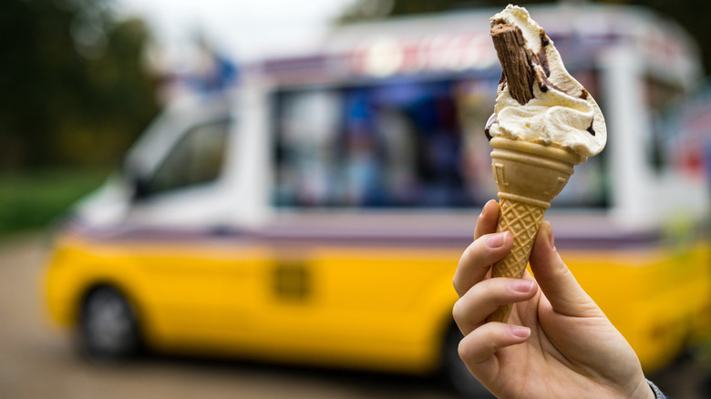 Person holding ice cream cone in front of ice cream truck