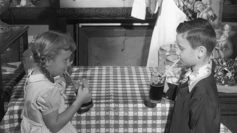 Two children drink root beer from glasses circa 1950
