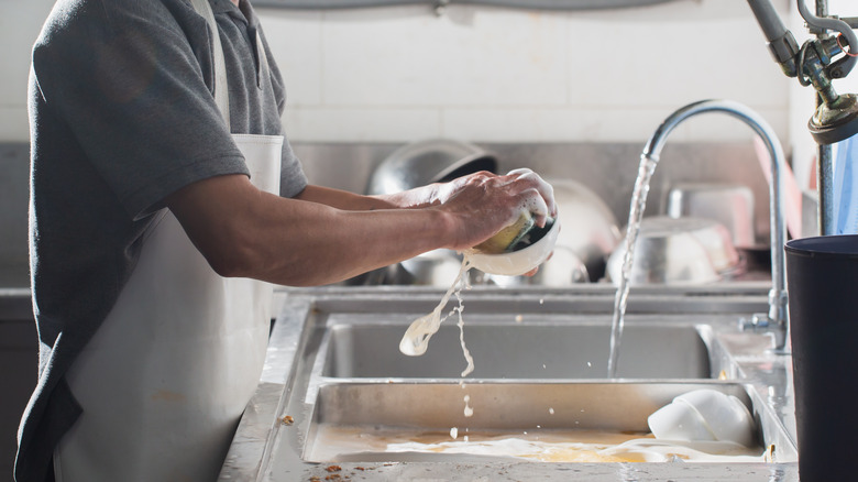 person washing dishes with sponge over the sink