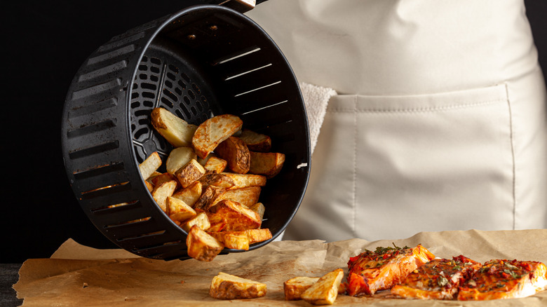 pouring fries out of an air fryer next to salmon