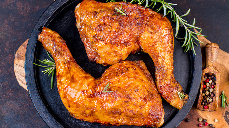 chicken legs in a black dish with a sprig of rosemary