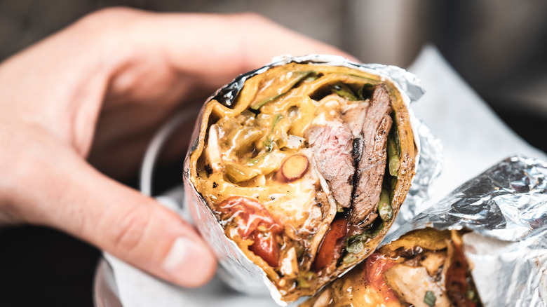 Hand holding burrito with cheese and meat