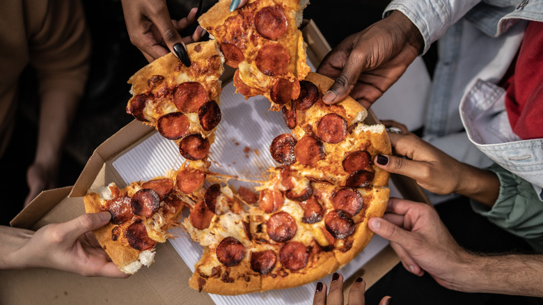 people grabbing sliced of pepperoni pizza