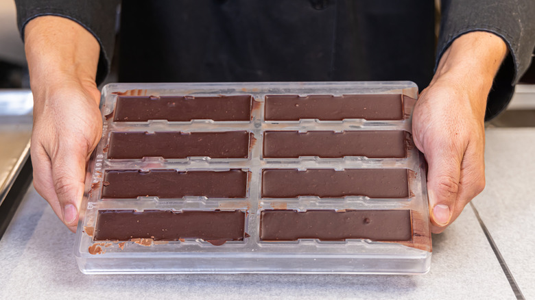 Hands holding a clear mold filled with hardened chocolate bars