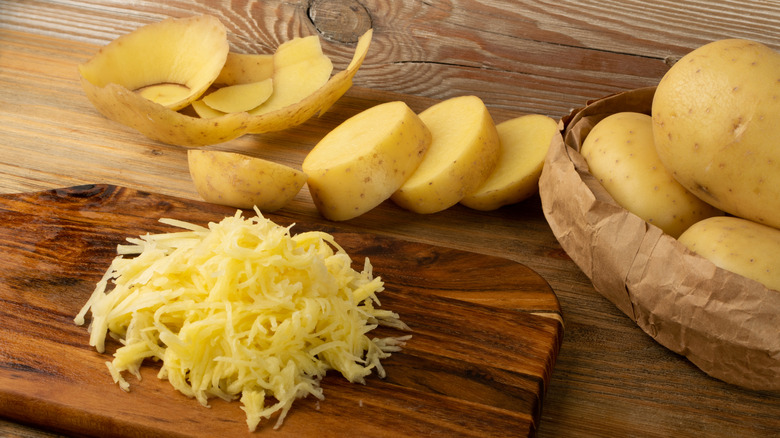 Grated potatoes, potato peels, and whole potatoes on a wooden surface