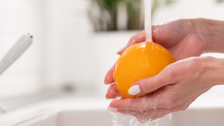 Person washing orange in sink