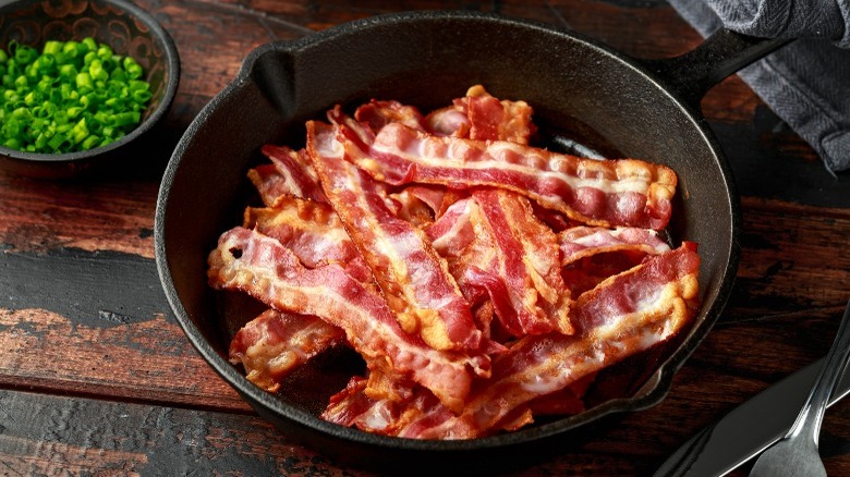 Cast iron pan filled with crisp bacon and a side of chopped green onions