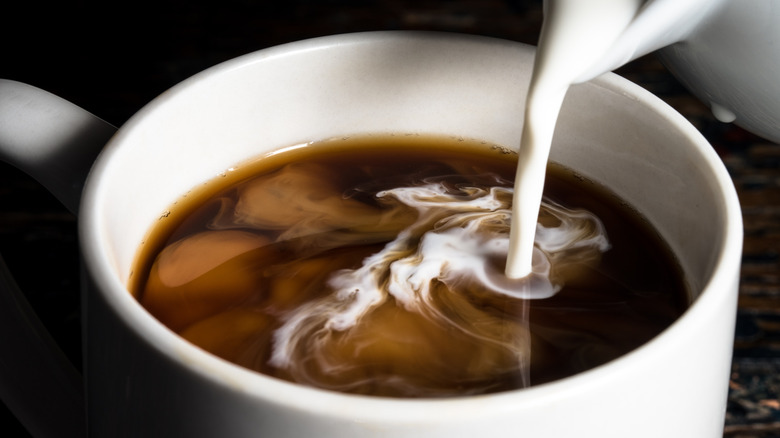 close up of pouring milk into black coffee