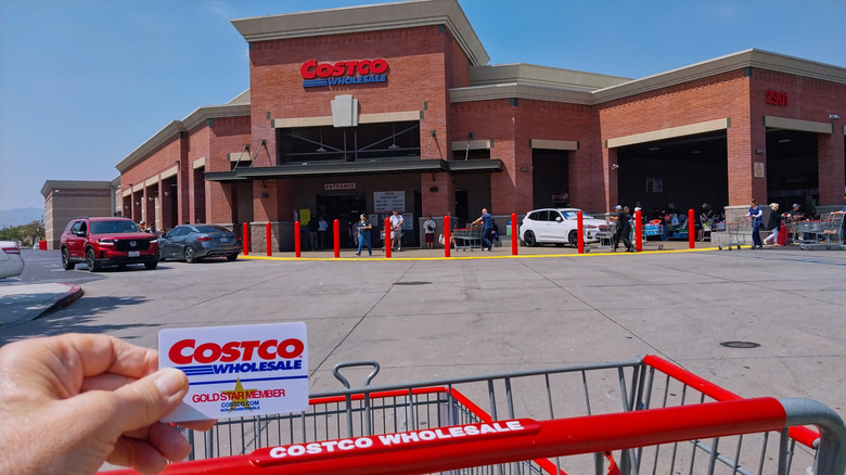 Hand holding Costco card in front of store