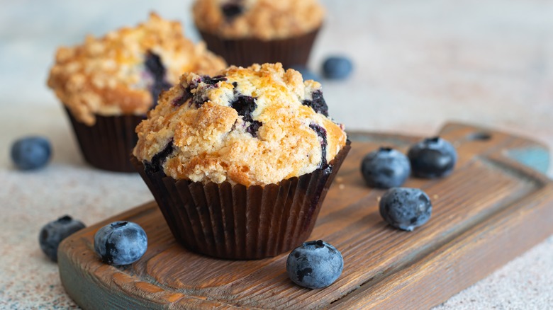 A blueberry muffin and blueberries on a cutting board