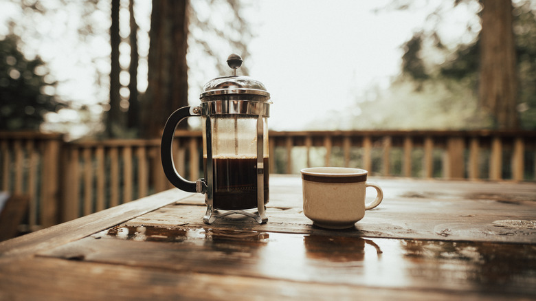 french press and coffee cup on wooden table