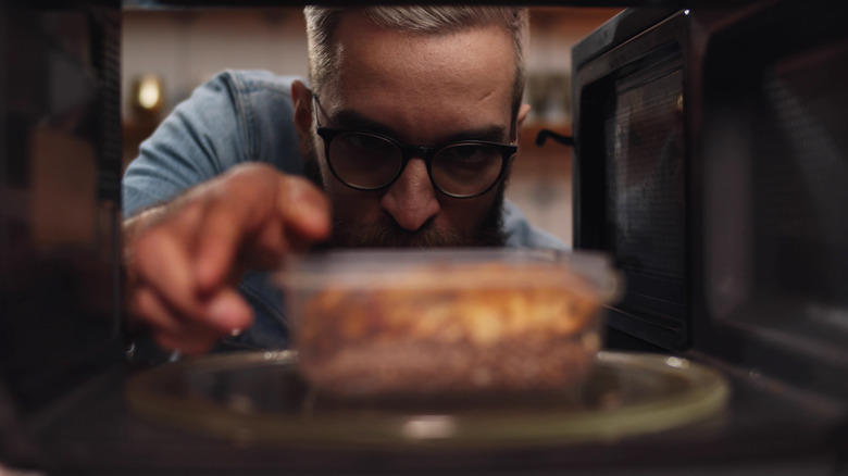 bearded man with glasses reaching into microwave