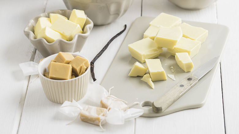 Butter, vanilla bean, and white chocolate chunks on cutting board with knife