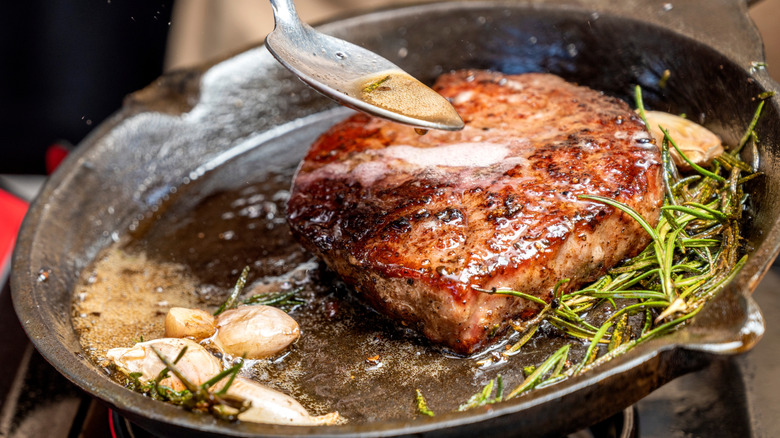 Basting steak in herb garlic butter in cast iron pan